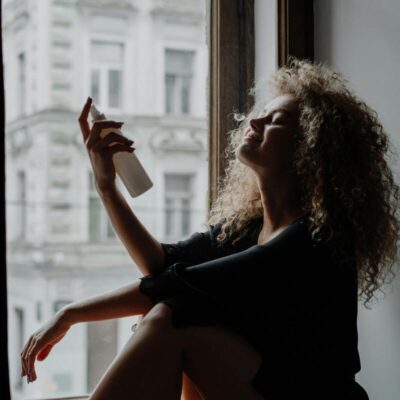 donna seduta alla finestra con gambe accavallate che utilizza uno spray