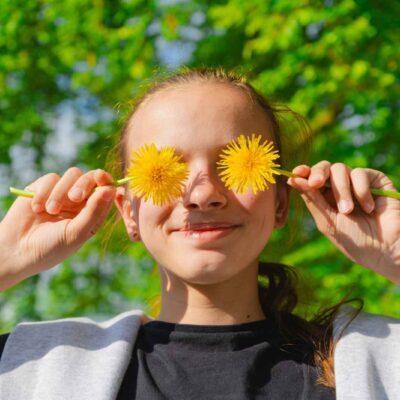 Ragazza in giardino che gioca con dei denti di leone