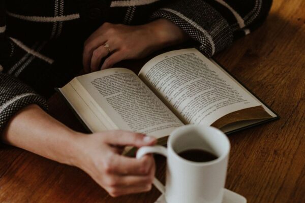 Mani accanto a un libro aperto sul tavolo e una tazza di caffè.