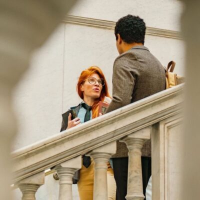 Una donna con alcuni libri in mano e un uomo con uno zaino sulla spalla conversano lungo una scalinata